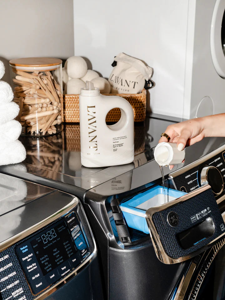 L’AVANT Collective Fresh Linen Laundry Detergent being poured into a washing machine detergent dispenser