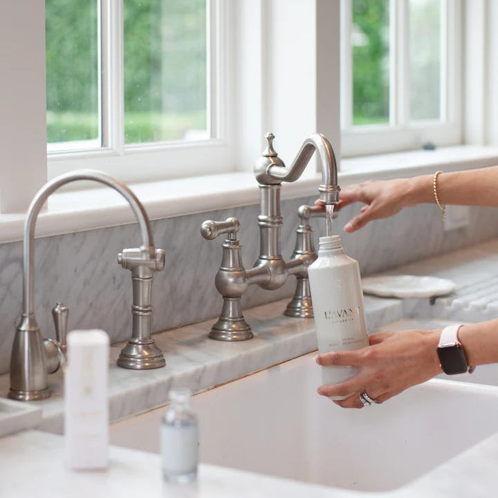 L’AVANT Fresh Linen multipurpose cleaner bottle being filled with water at a kitchen sink after adding concentrate