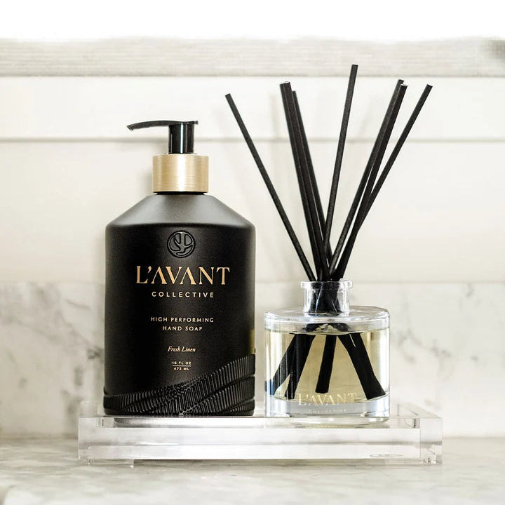 L’AVANT Collective Fresh Linen reed diffuser styled with coordinating luxury hand soap on a clear countertop tray.