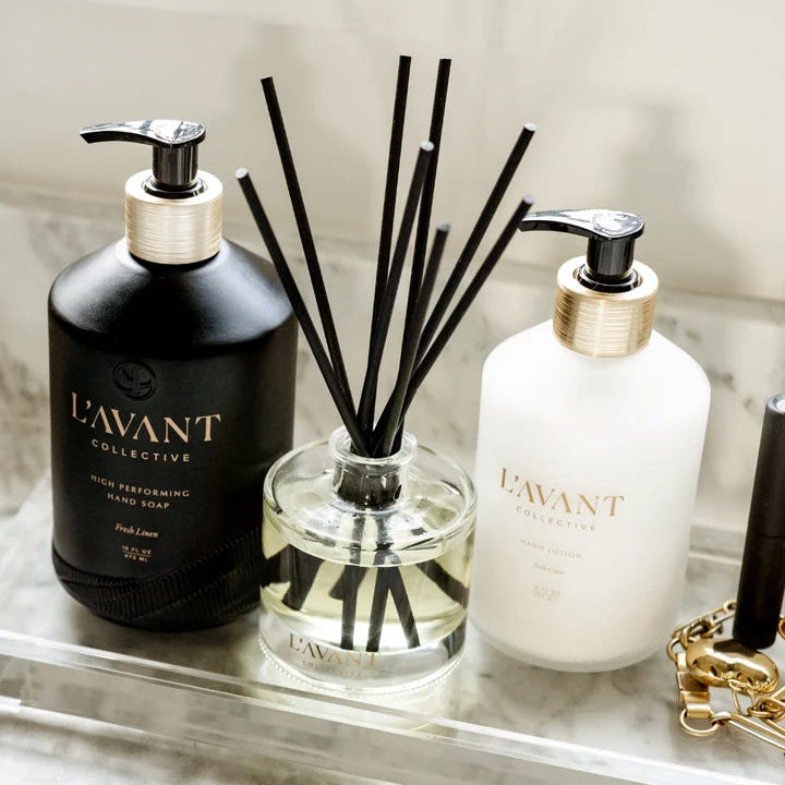 L’AVANT Collective Fresh Linen reed diffuser styled with coordinating hand soap and hand lotion on a clear tray.