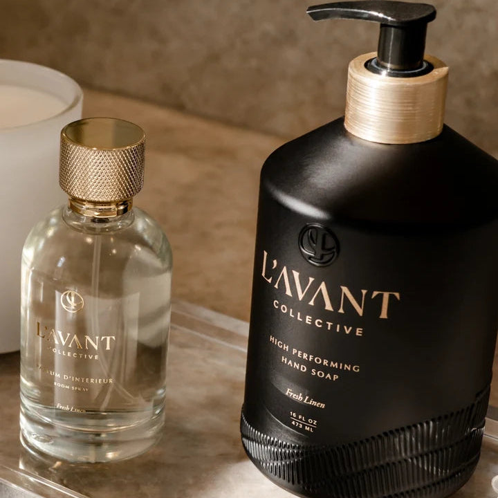 L’AVANT Collective Fresh Linen Room Spray displayed beside coordinating black Fresh Linen hand soap on a clear countertop tray.