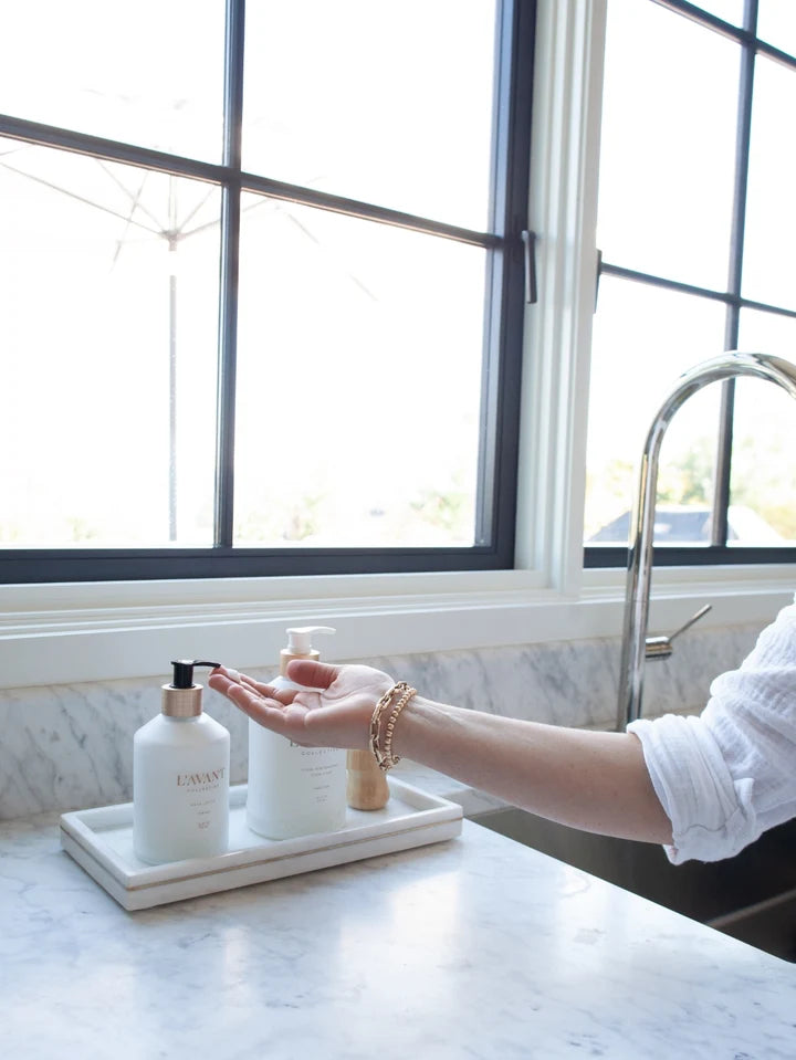 L’AVANT Collective Hand Lotion displayed beside coordinating sink care products on a marble kitchen countertop
