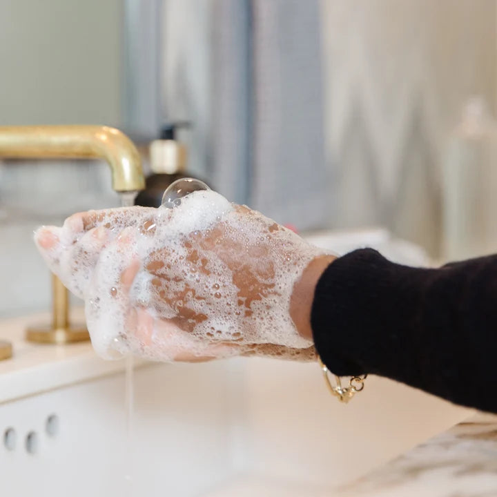 Hands washing with rich foamy lather from L’AVANT Collective High Performing Hand Soap at a bathroom sink