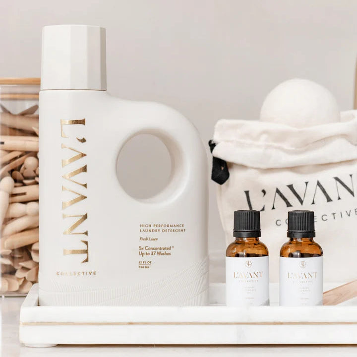 L’AVANT Collective Fresh Linen laundry detergent styled with wool dryer balls, laundry oil drops, and reusable laundry accessories.