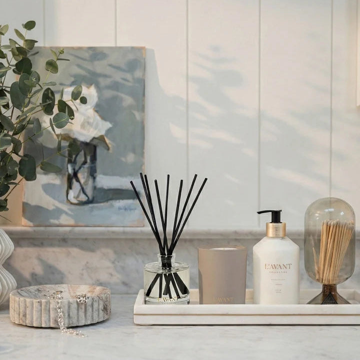 L’AVANT Collective luxury reed diffuser displayed with coordinating candle and hand lotion on a marble countertop.