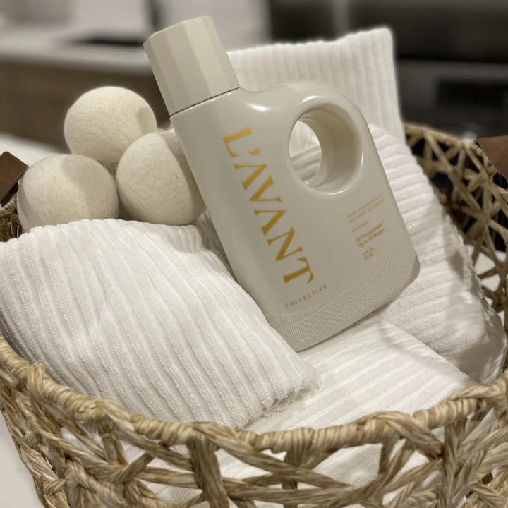 L’AVANT Wool Dryer Balls and high performance laundry detergent styled with fresh white towels in a woven basket.