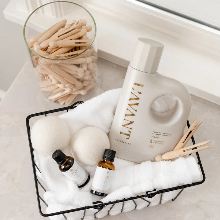 L’AVANT Wool Dryer Balls styled with laundry detergent, fragrance oils and fresh white towels in a laundry basket.