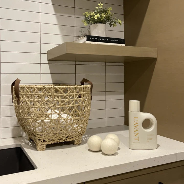 L’AVANT Wool Dryer Balls displayed beside laundry detergent and a woven laundry basket in a modern laundry room.