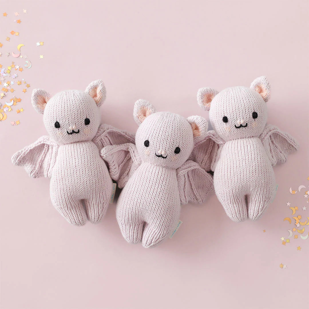 Three lavender knitted baby bat stuffed animals displayed on a pink background