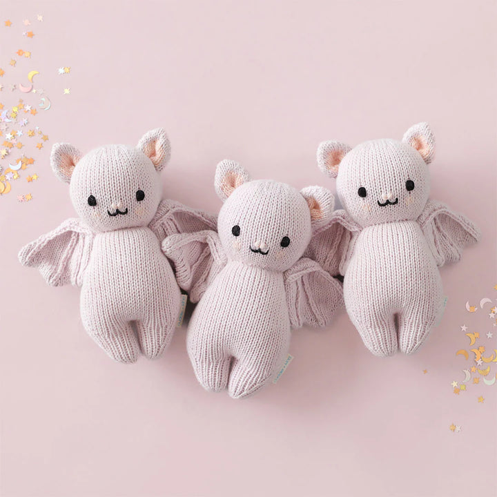 Three lavender knitted baby bat stuffed animals displayed on a pink background