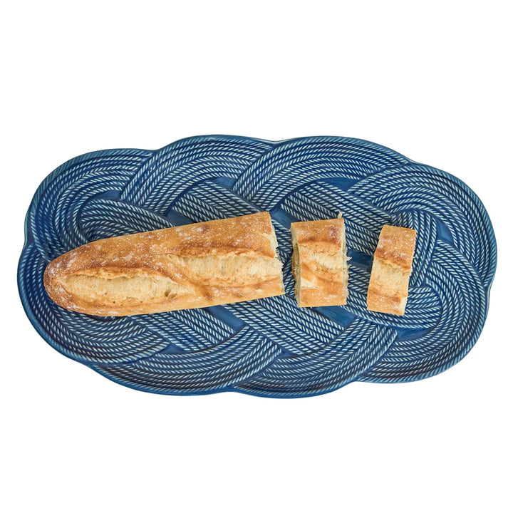 Angled view of the Le Panier Mystic Knot Hostess Tray in Denim showcasing woven detailing and a sculptural blue knot accent.