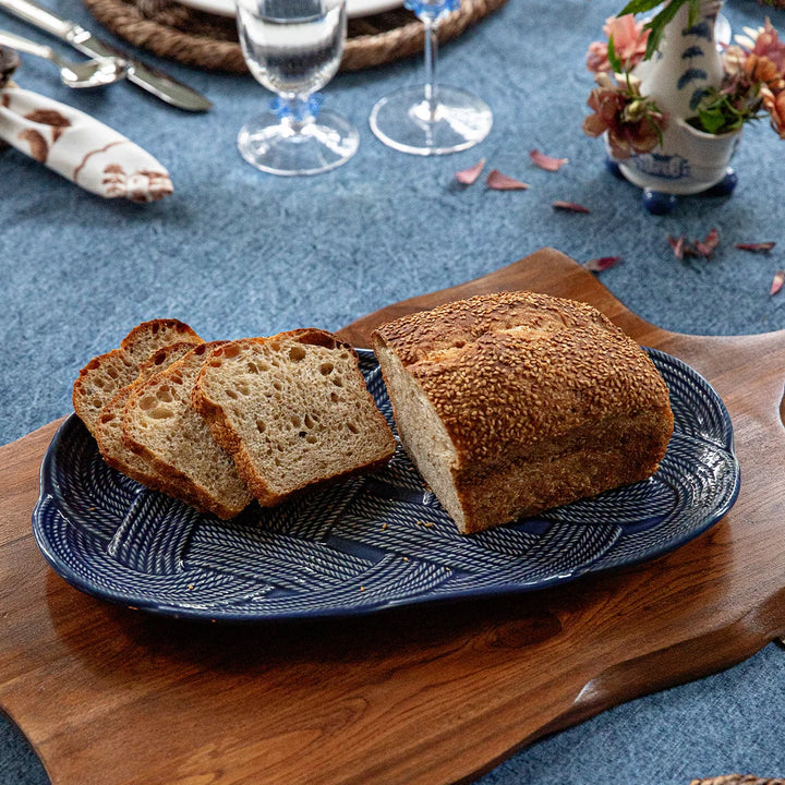 Le Panier Mystic Knot 15-inch Hostess Tray in Denim styled for serving with its woven border and decorative blue knot detail.