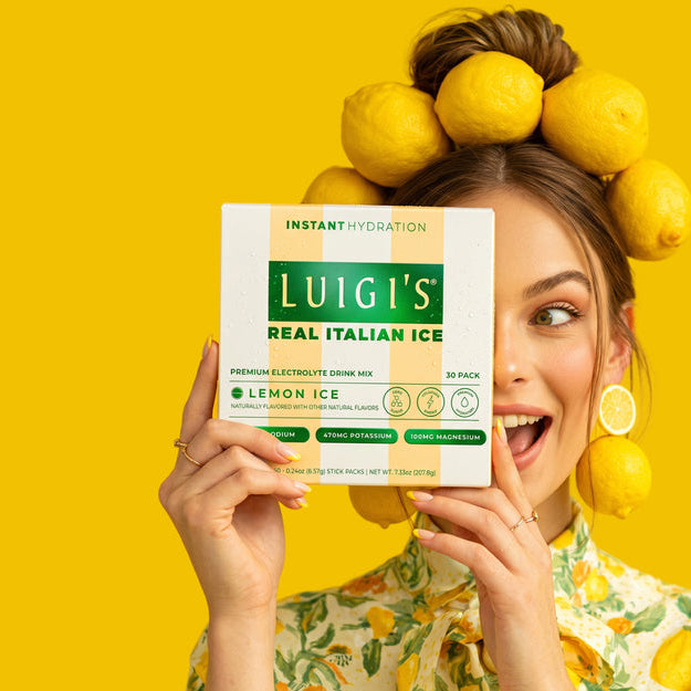 Luigi’s Lemon Ice Electrolyte Drink Mix 30-pack held beside fresh lemons against a bright yellow background