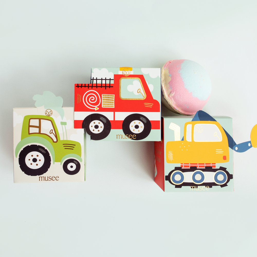 Musee's excavator themed bath balm, displayed next to the box the tractor and firetruck themed balm balm boxes.