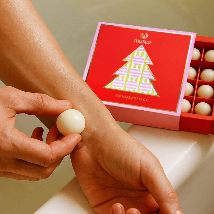 Lifestyle image of a woman using the Holiday Body Melt Set to moisturize her wrist over water. 