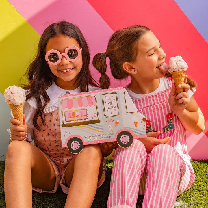 Two girls enjoying ice cream while holding a Musee ice cream truck bath balm and accessory set.