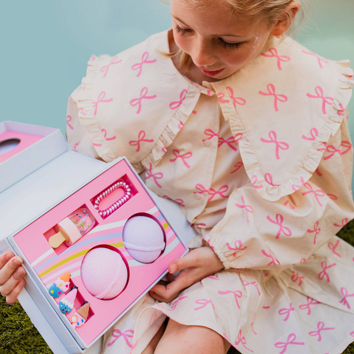 Young girl holding an open Musee ice cream truck bath balm and accessory set featuring two bath balms, lip gloss, a hair tie, and ice cream hair clips.