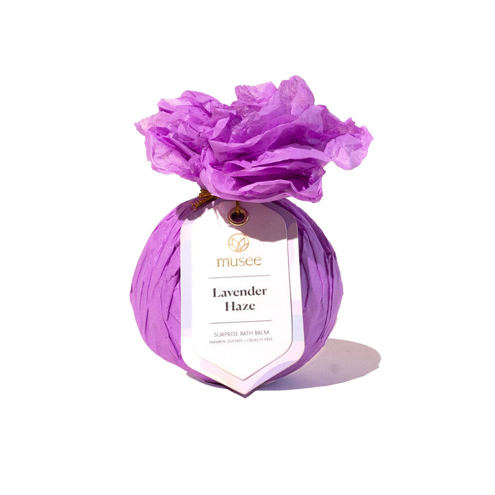 Musee Lavender Haze surprise bath balm wrapped in a bright violet paper with a decorative product tag.