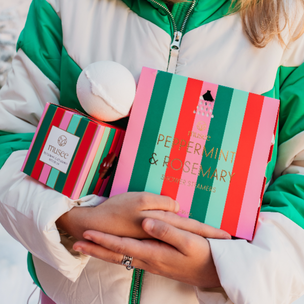 Individual holding Musee's Peppermint and Rosemary Shower Steamers, and the Luxe Bath Balm in their arms. 