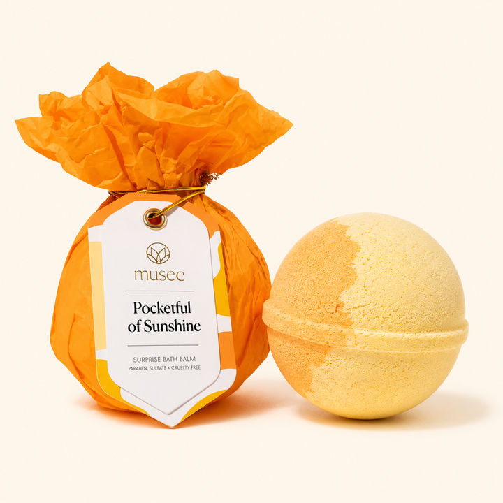 Musee Pocketful of Sunshine surprise bath balm shown beside its orange tissue-wrapped package.