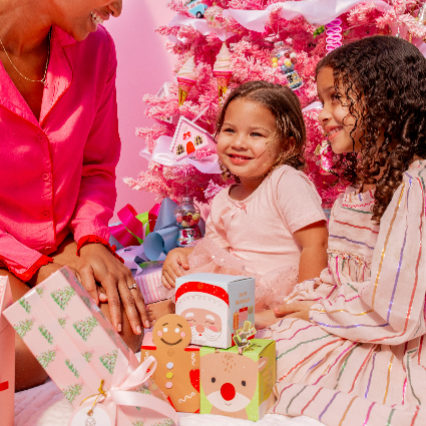 Lifestyle image of two little girls opening christmas gifts under a pink christmas tree, these gifts include Musee&