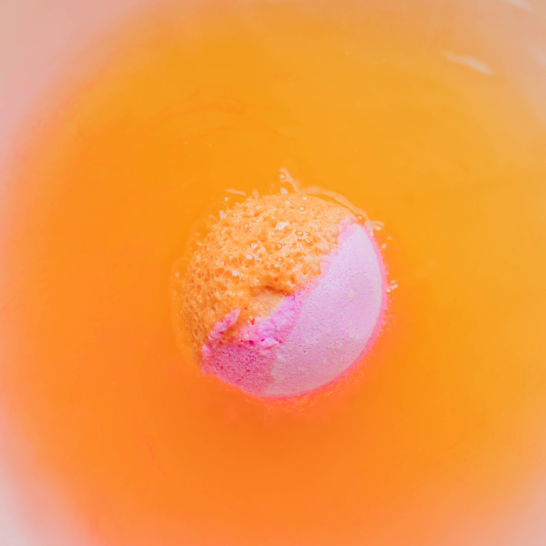 Musee Tiny Dancer surprise bath balm fizzing in water. Vibrant orange color taking over the once clear water.