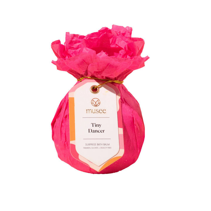 Musee Tiny Dancer surprise bath balm wrapped in bright pink tissue paper with a decorative product tag.
