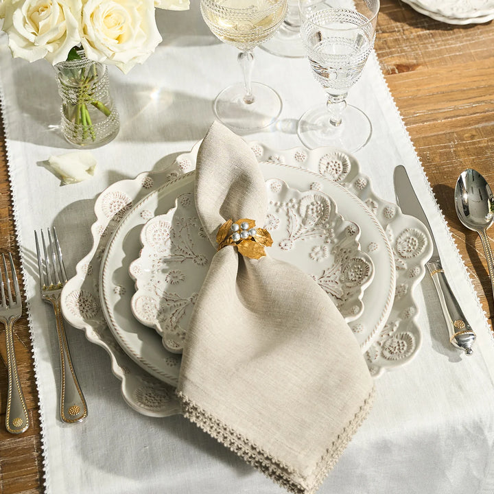 Natural linen napkin with crochet edge styled with a gold floral napkin ring, white dinnerware and glassware