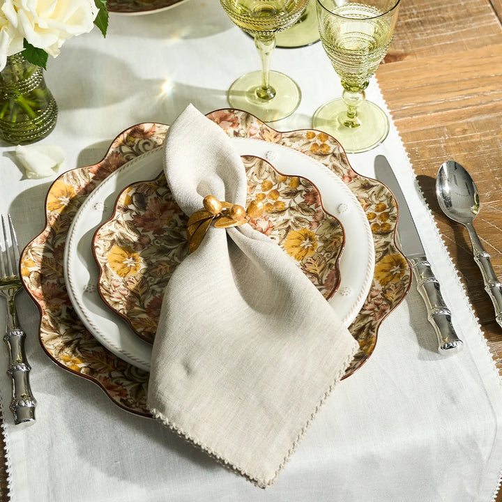 Natural linen napkin with crochet trim styled with a gold napkin ring and floral dinnerware on an elegant tablescape