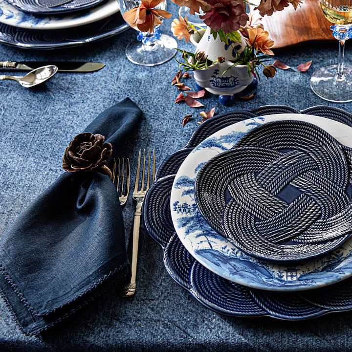 Navy blue linen napkin styled with blue and white dinnerware, woven chargers, florals and elegant table accessories