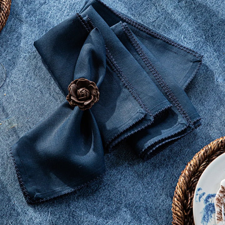 Navy blue linen napkins with crochet edging styled on a blue dining table with a decorative floral napkin ring