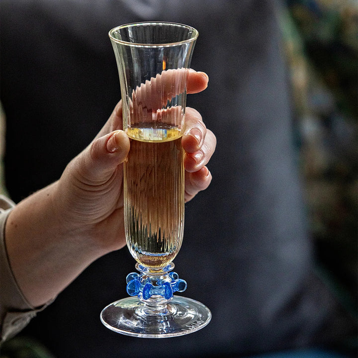 Nell Ruffle Flute in Chambray held in hand with champagne, showcasing the ribbed clear glass and decorative blue ruffle stem detail.