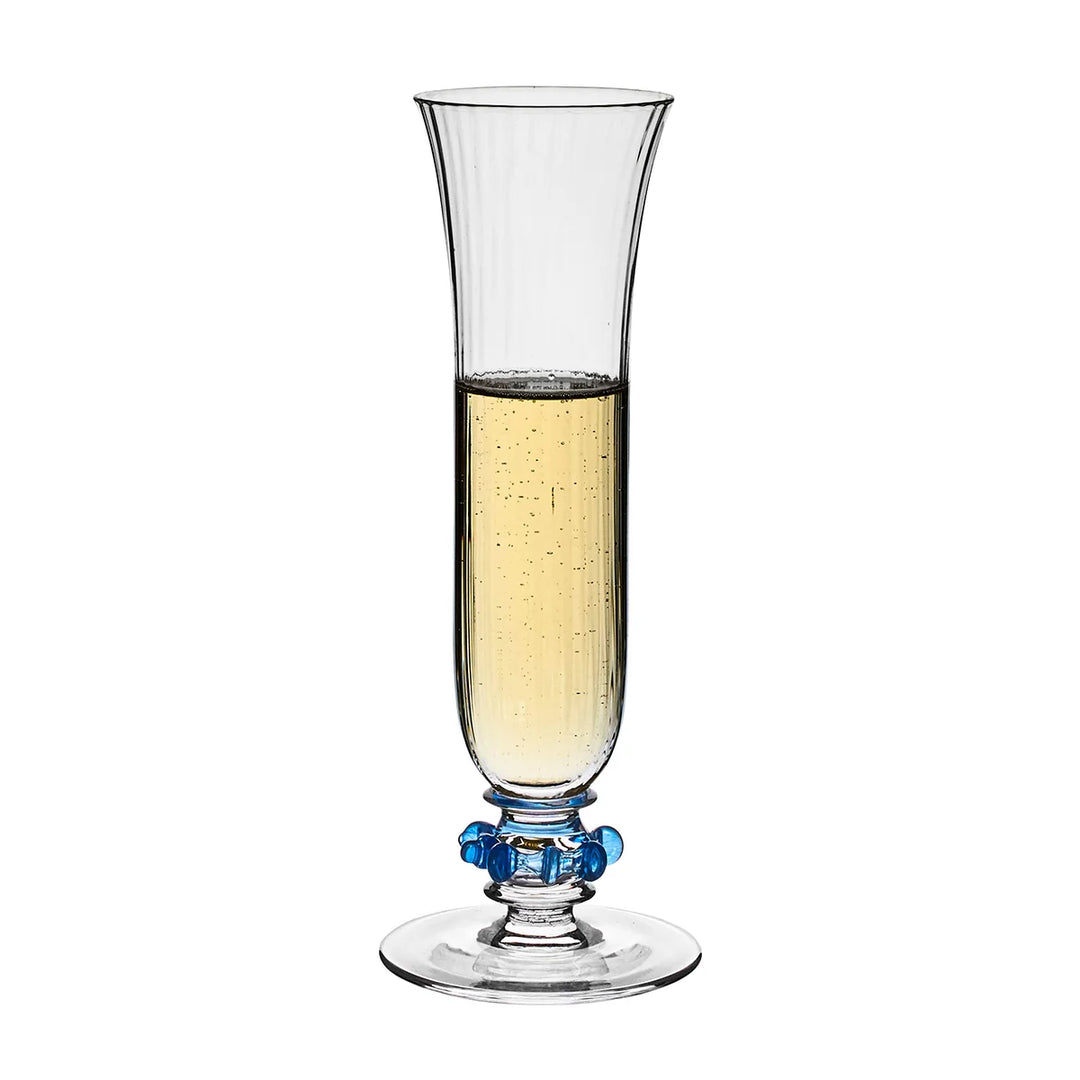 Nell Ruffle Flute in Chambray filled with champagne, featuring a tall ribbed glass bowl and signature blue ruffle glass accents.