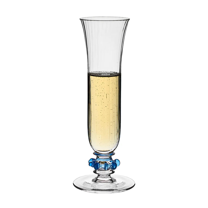 Nell Ruffle Flute in Chambray filled with champagne, featuring a tall ribbed glass bowl and signature blue ruffle glass accents.