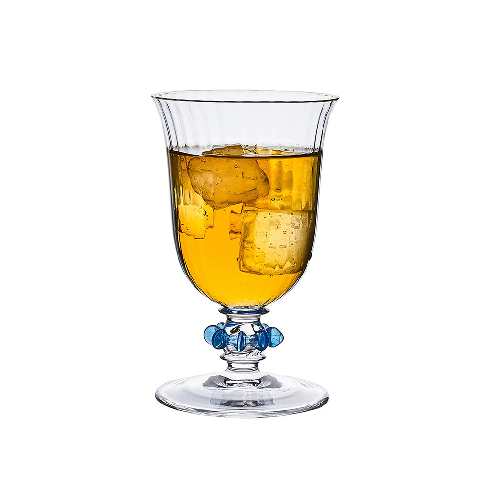 Nell Ruffle Goblet in Chambray filled with a beverage, showcasing a ribbed clear glass bowl and signature blue ruffle stem detail.