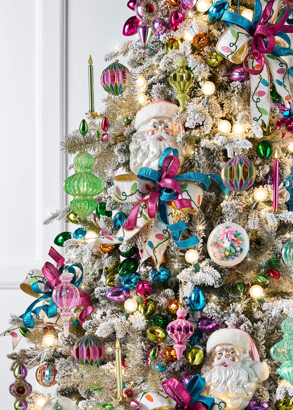 Cream embroidered neon Christmas light ribbon styled in bows on a flocked Christmas tree with pink and turquoise ribbon, colorful ornaments, Santa decorations and glowing lights.