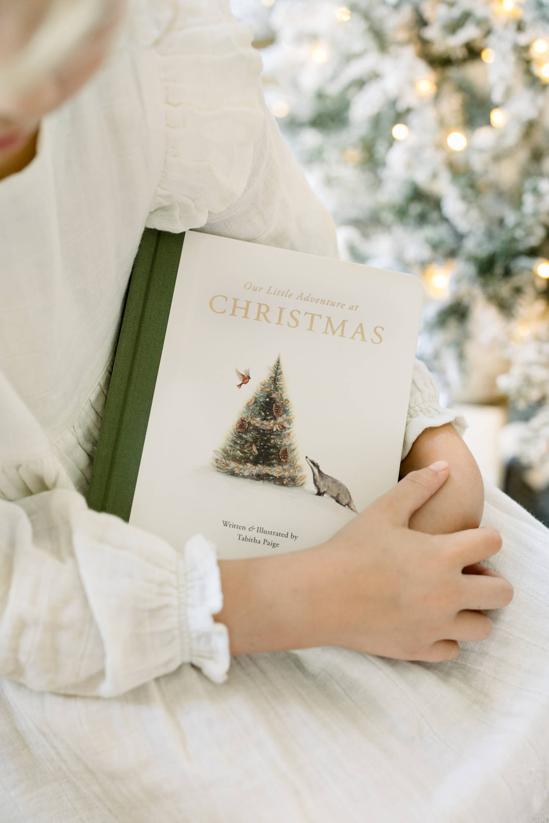 Child holding Our Little Adventure at Christmas by Tabitha Paige in front of a decorated Christmas tree