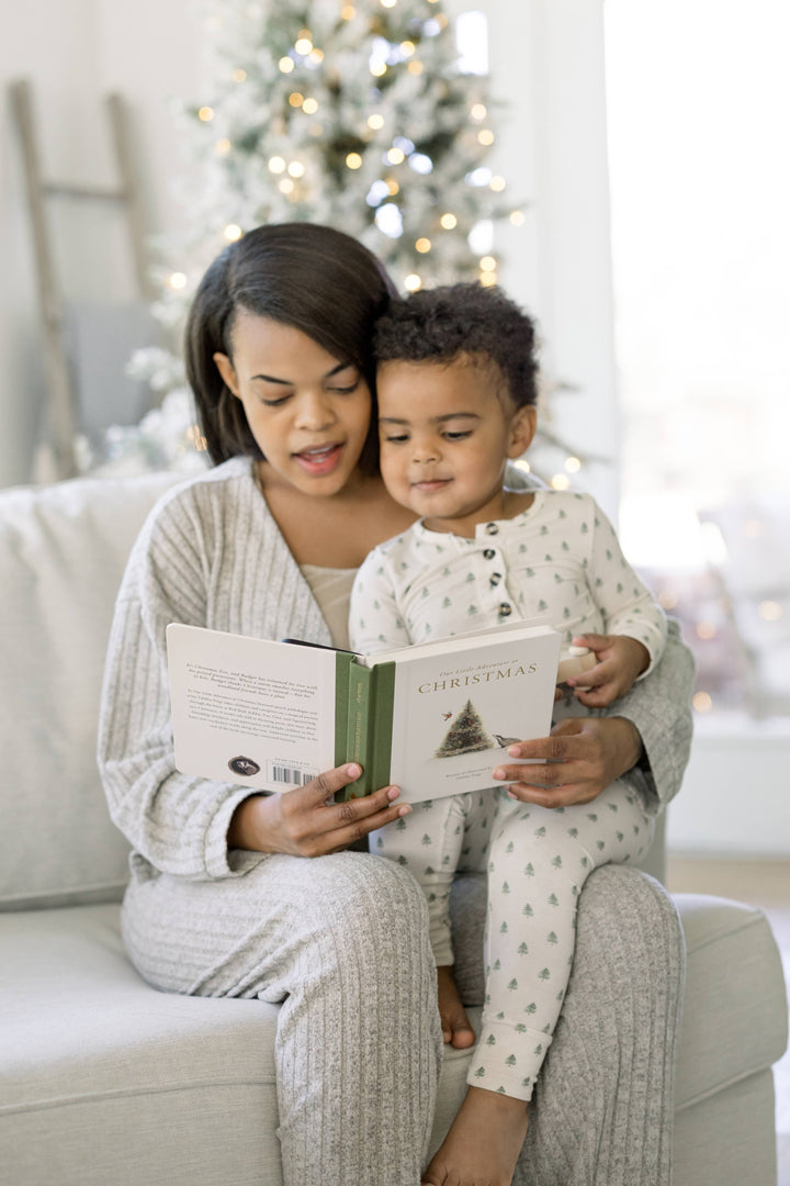 Parent reading Our Little Adventure at Christmas with a young child beside a decorated Christmas tree
