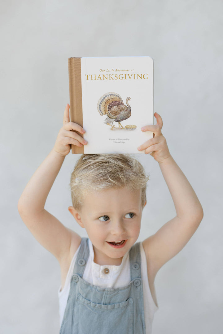 Young child holding Our Little Adventure at Thanksgiving above his head