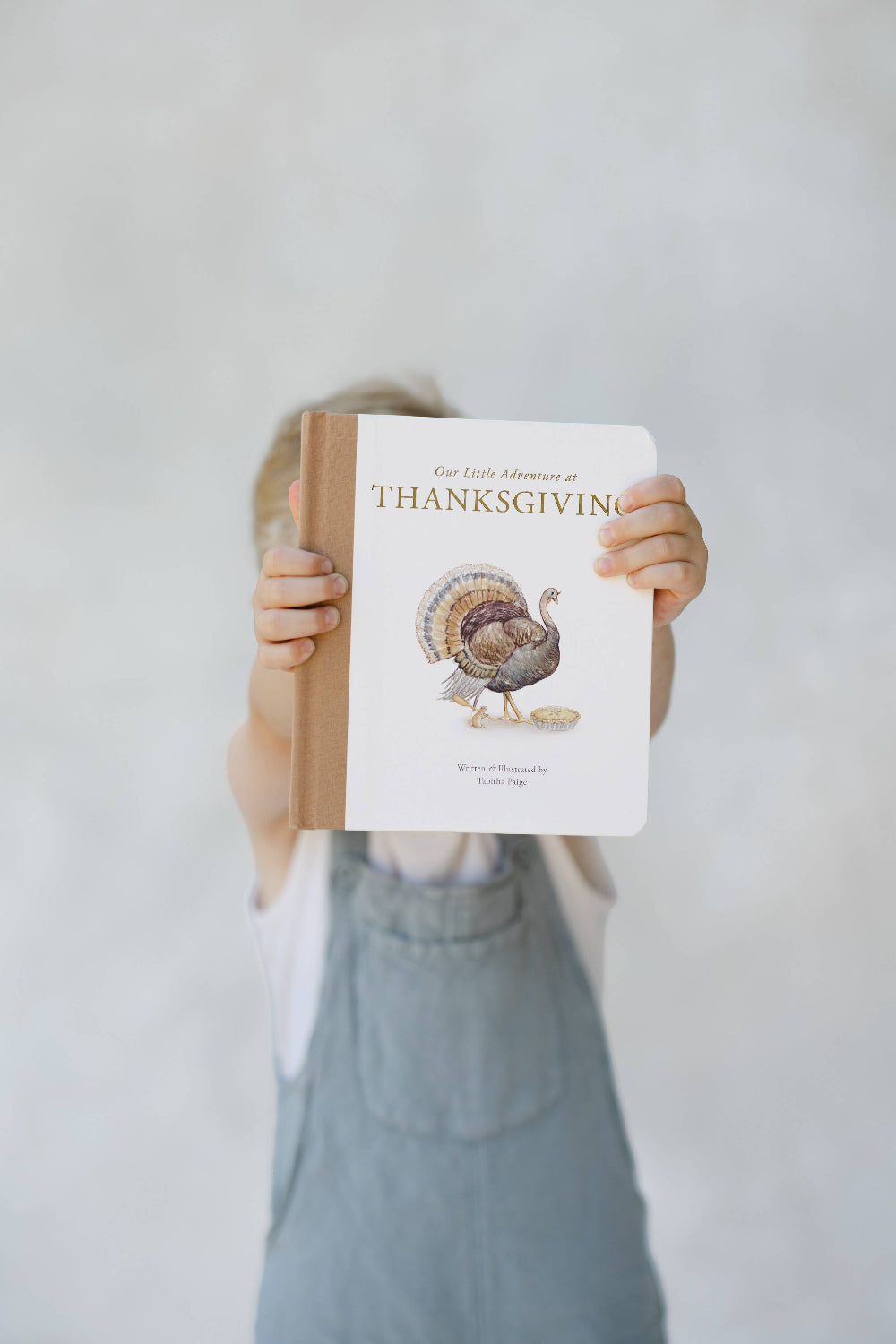 Young child holding Our Little Adventure at Thanksgiving in front of his face