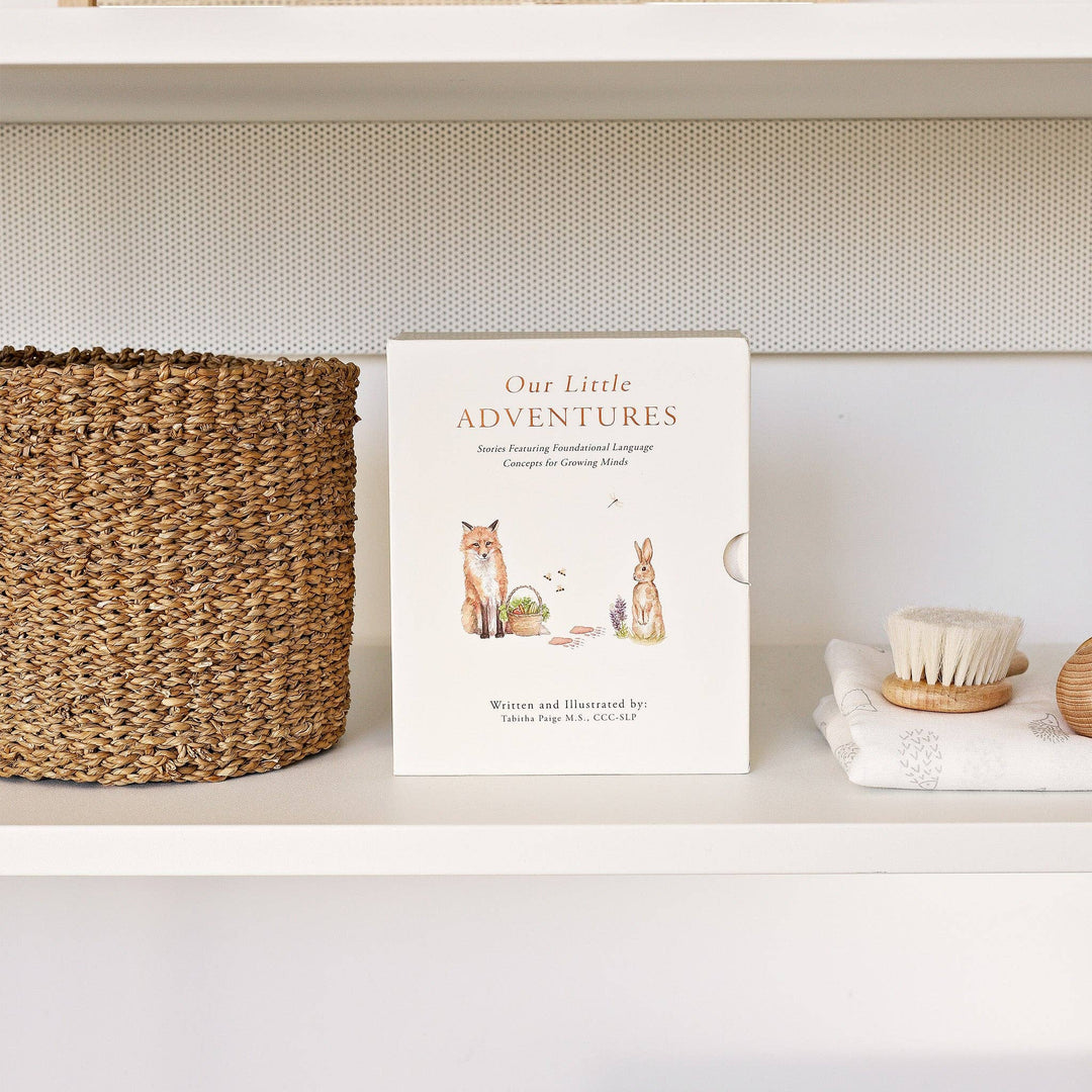 Our Little Adventures board book box set displayed on a nursery shelf beside a woven basket and baby brush