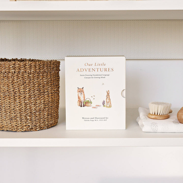 Our Little Adventures board book box set displayed on a nursery shelf beside a woven basket and baby brush