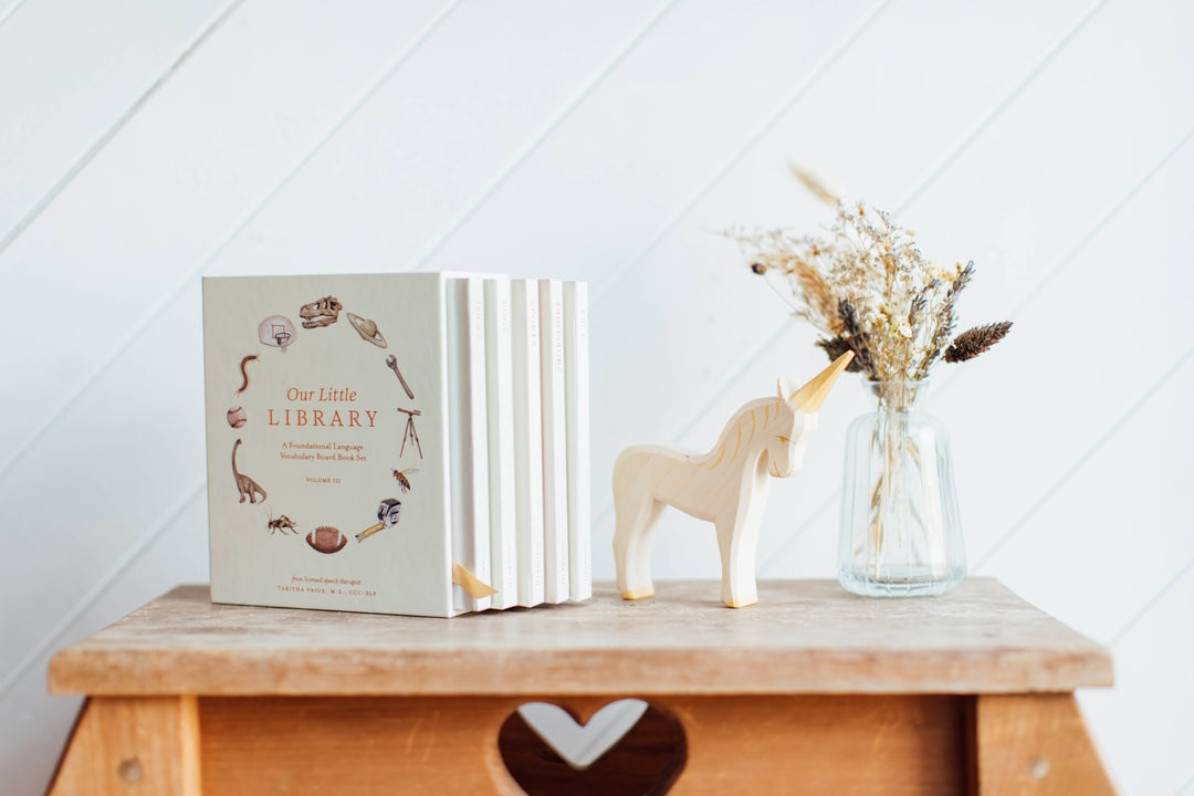 Our Little Library Vol. 3 five board book set displayed with its slipcase, wooden unicorn, and dried flowers