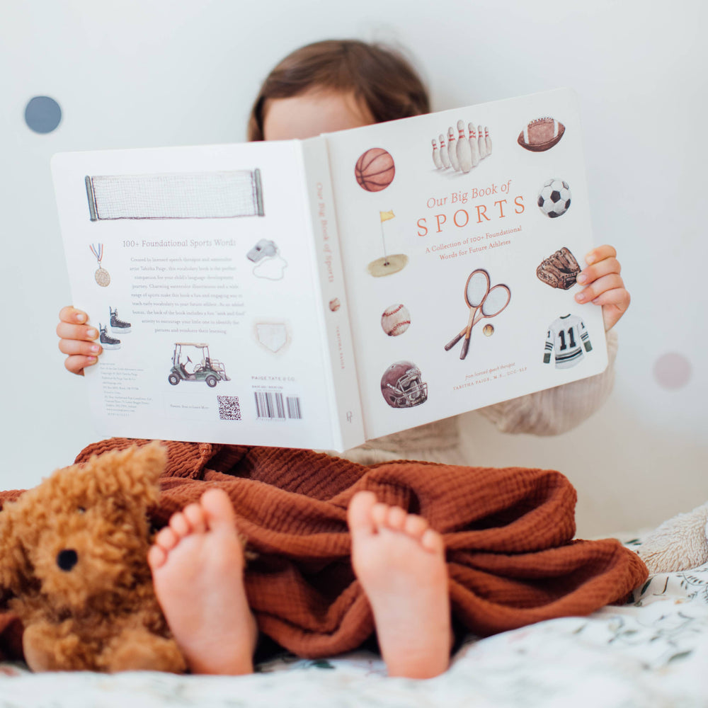 Styled image of Paige Tate & Co.'s Our Big Books of Sports, featuring the book being red by a child. 