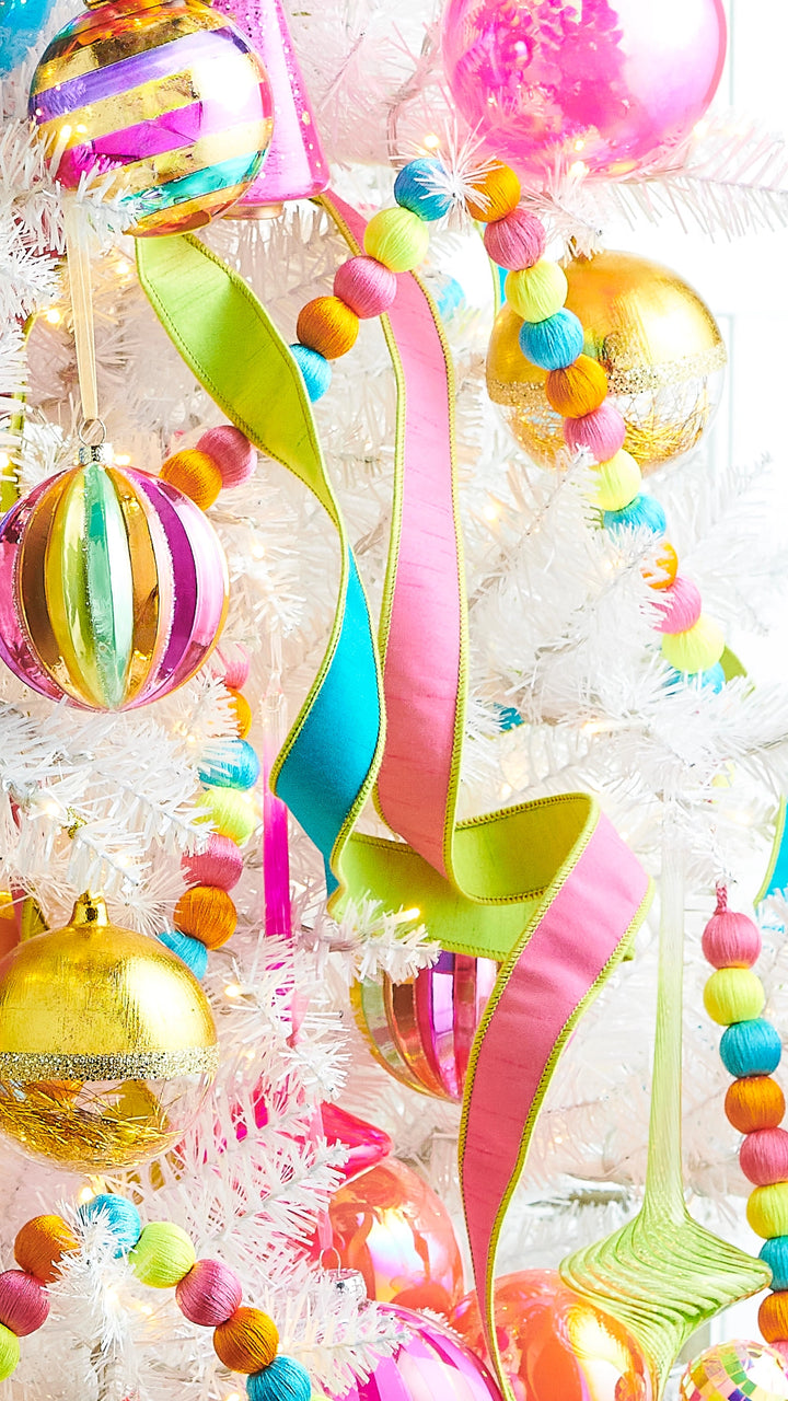 Pink and lime green reversible wired ribbon cascading through a colorful white Christmas tree decorated with bright ornaments and multicolor ball garland.