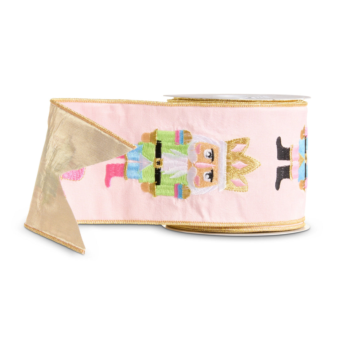 Light pink wired Christmas ribbon featuring colorful embroidered nutcracker characters in pink, blue, green and gold, finished with metallic gold wired edges and a gold reverse.
