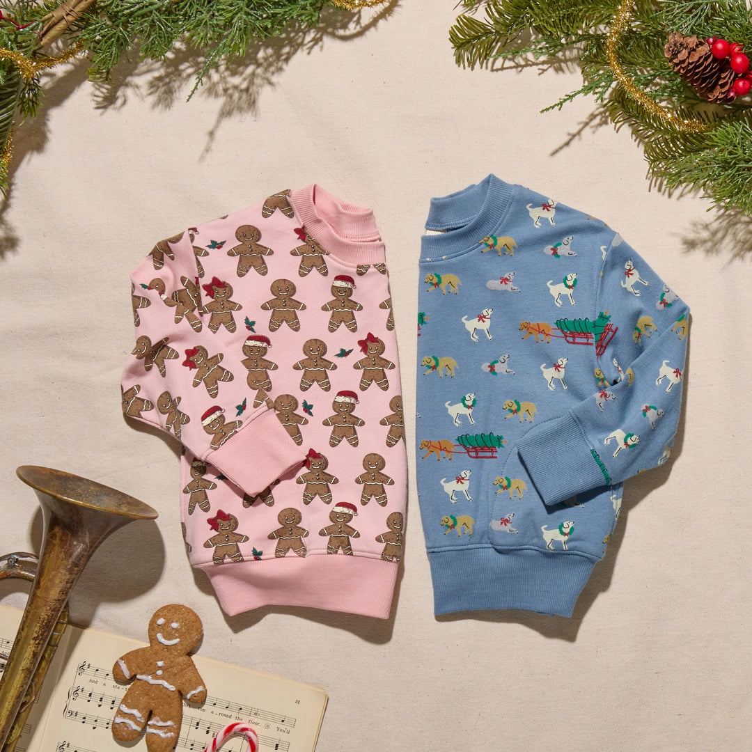 Blue Holiday Labs Play Sweatshirt displayed beside a pink gingerbread sweatshirt with festive Christmas greenery and holiday decorations.