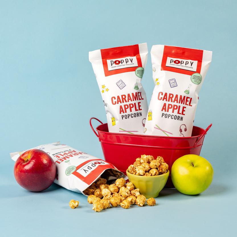 Poppy Caramel Apple Popcorn bags arranged in a red bucket with caramel popcorn and fresh apples.