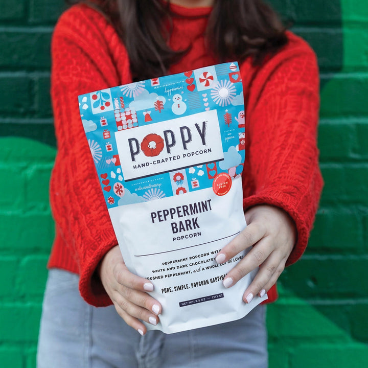 Woman holding Poppy Peppermint Bark Popcorn in colorful Christmas packaging