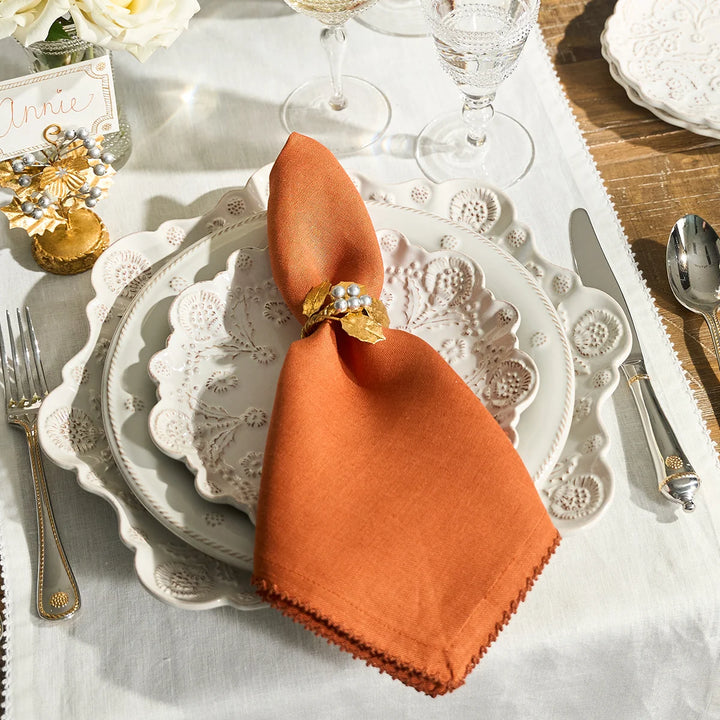Rust linen napkin styled with a gold berry napkin ring on an elegant white dinnerware place setting
